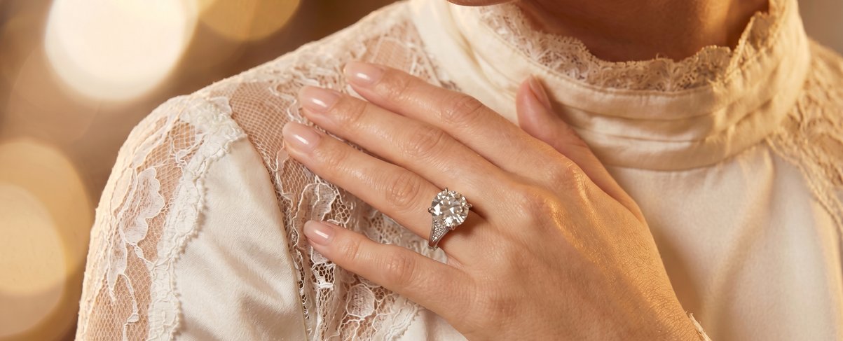 Bride's hand with an engagement ring resting on a lace wedding dress